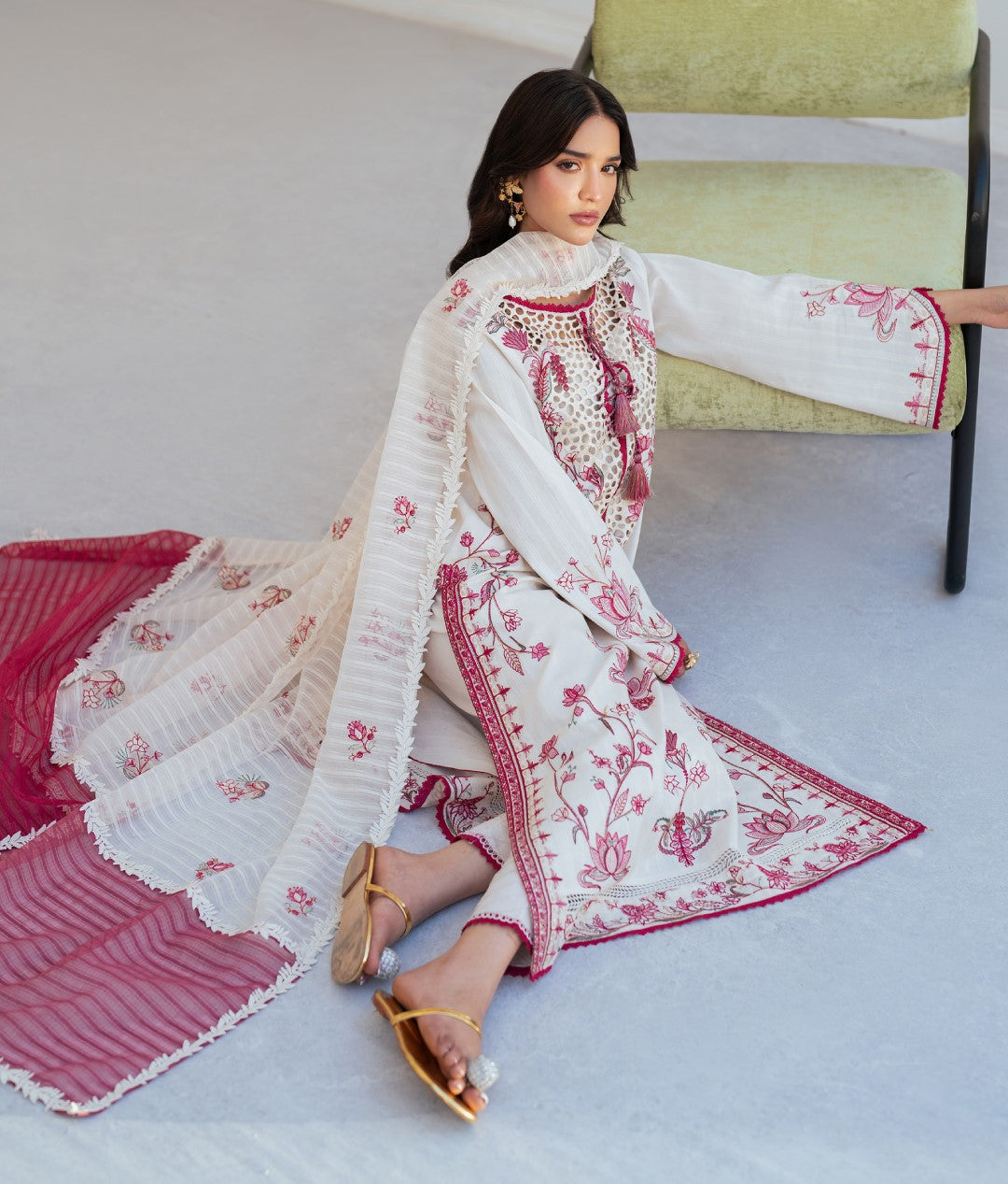 Woman in a white and red embroidered traditional outfit sitting on a chair.