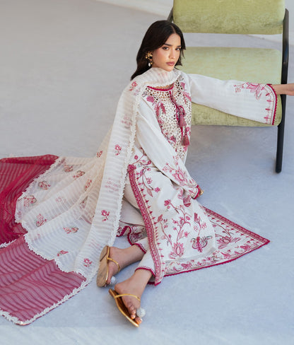Woman in a white and red embroidered traditional outfit sitting on a chair.